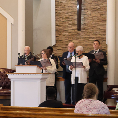 Choir singing hymns from hymnals on platform during Calvary Bible Baptist Church worship service